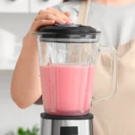 Person pressing the blender lid onto a glass blender filled with pink smoothie.