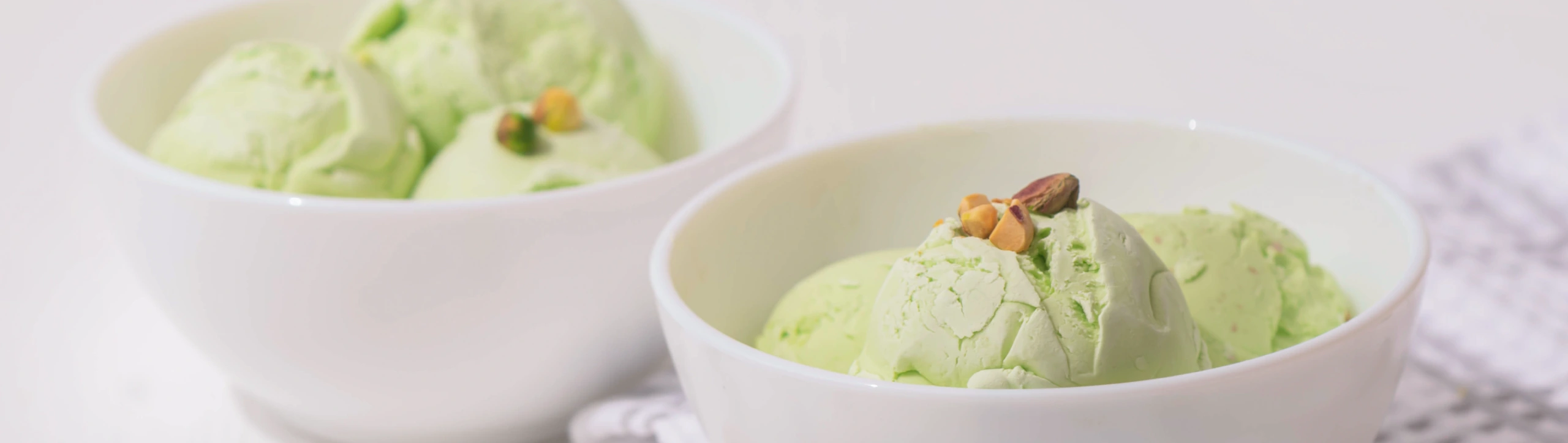 Two white bowls of pistachio ice cream with chopped nuts on top.