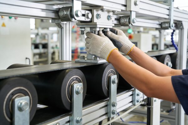 Gloved hands tighten bolts on a metal framework of an industrial machine in a factory setting